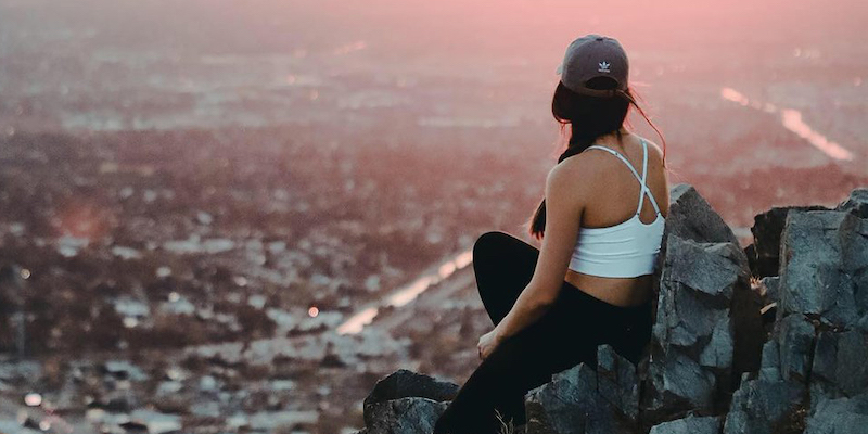 young woman sitting on a cliff overlooking the valley young woman sitting on a cliff overlooking the valley